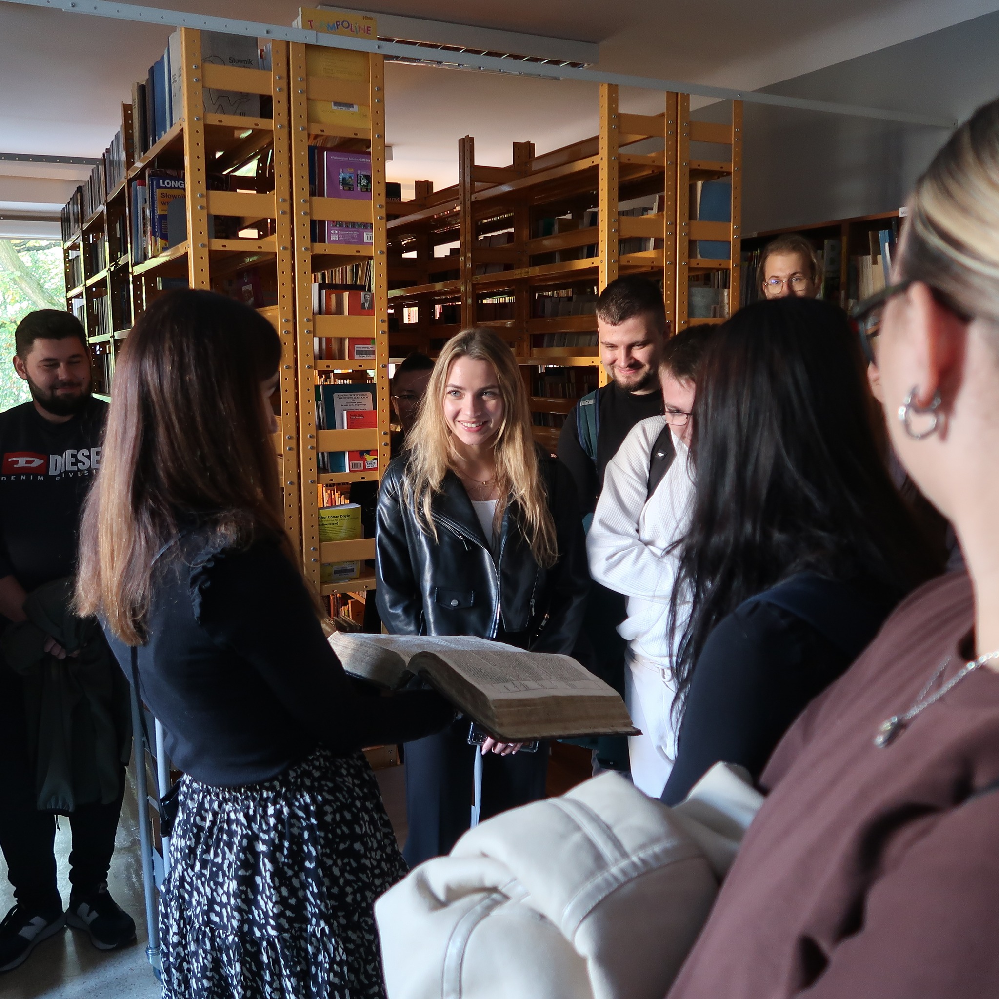 Młodzież ogląda zabytkowe książki w magazynie bibliotecznym.