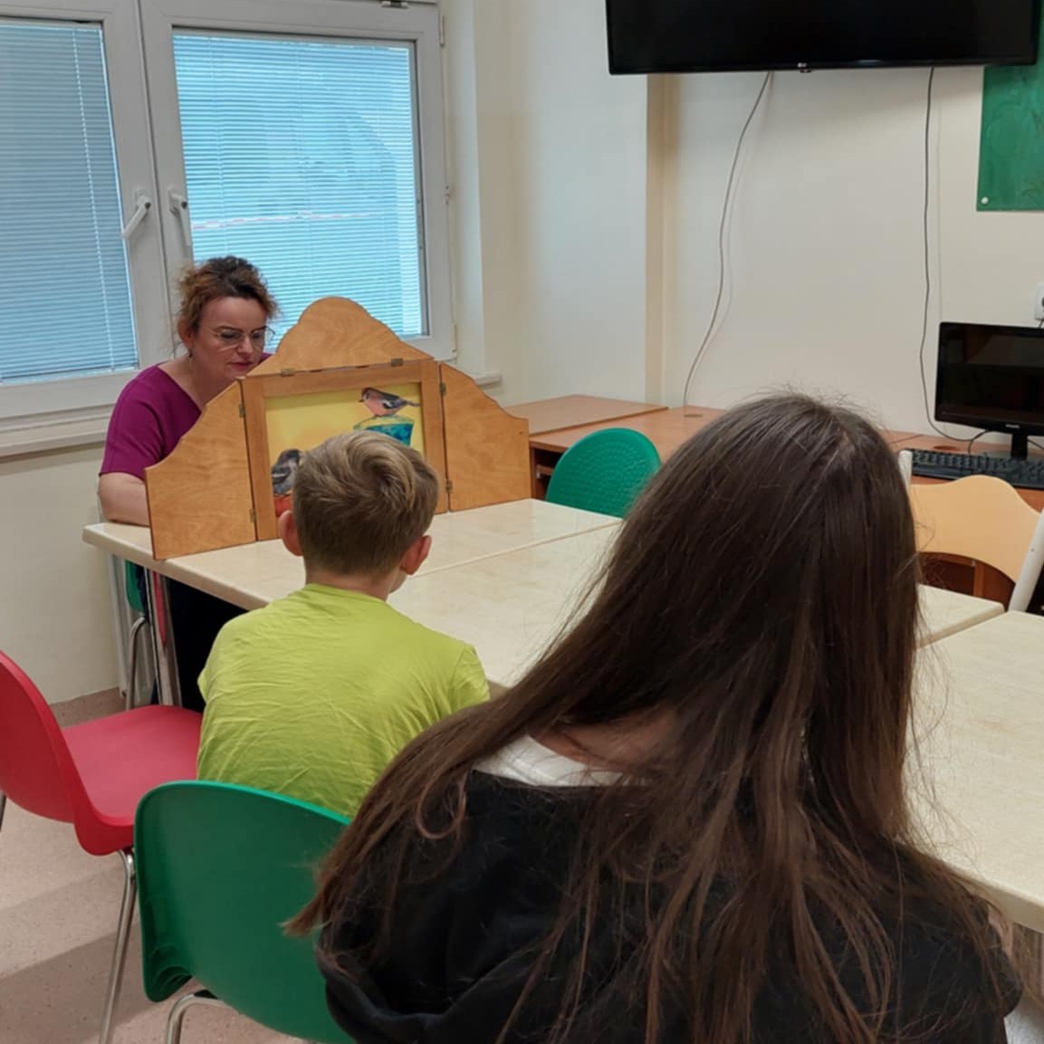 Dzieci słuchają opowieści z teatrzyku kamishibai.