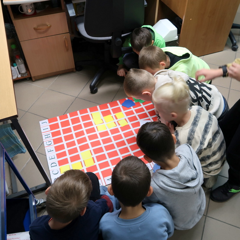 Dzieci próbują odczytać zakodowany znak na planszy rozłożonej na podłodze.