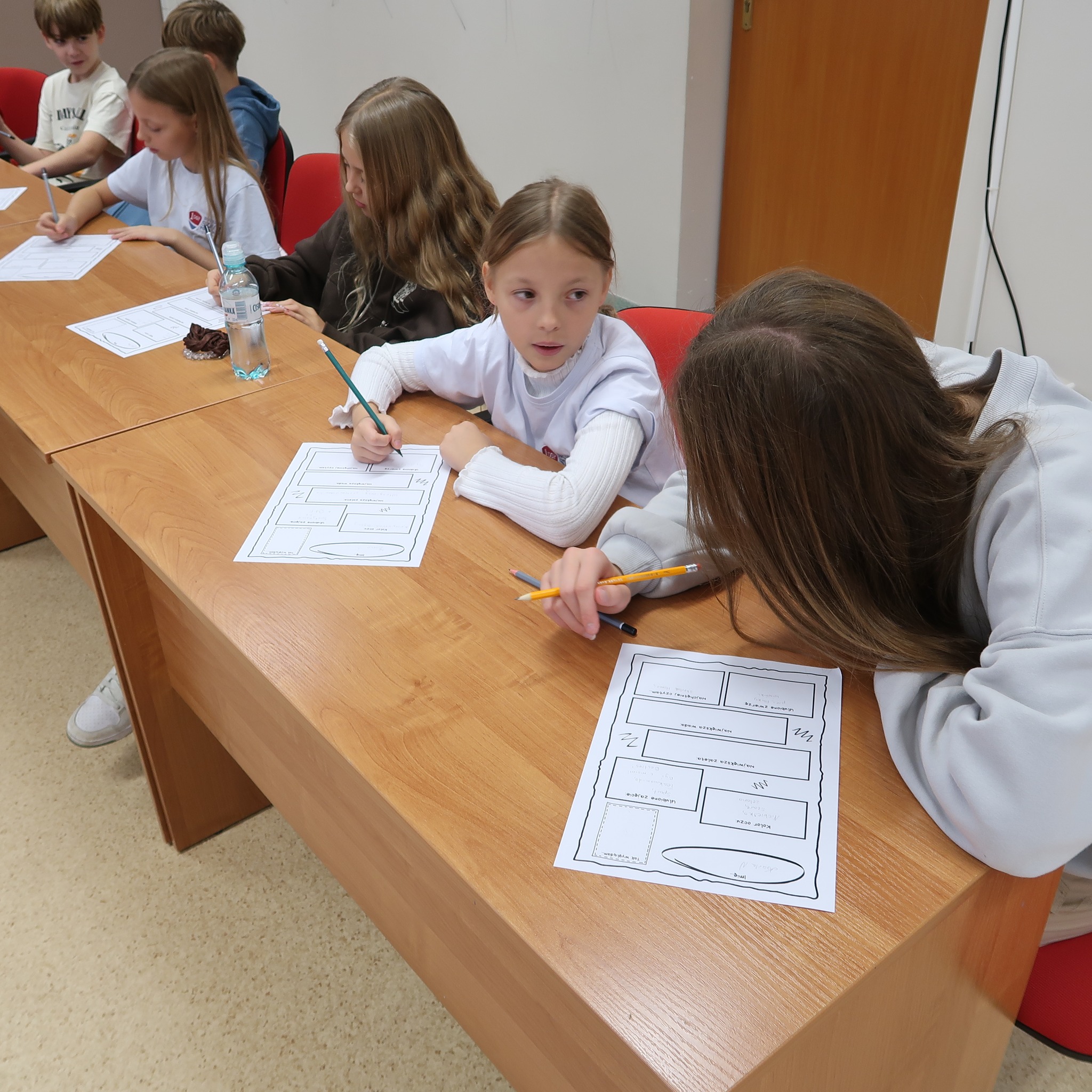 Dzieci siedząc przy stołach pracują w grupach nad zadaniem